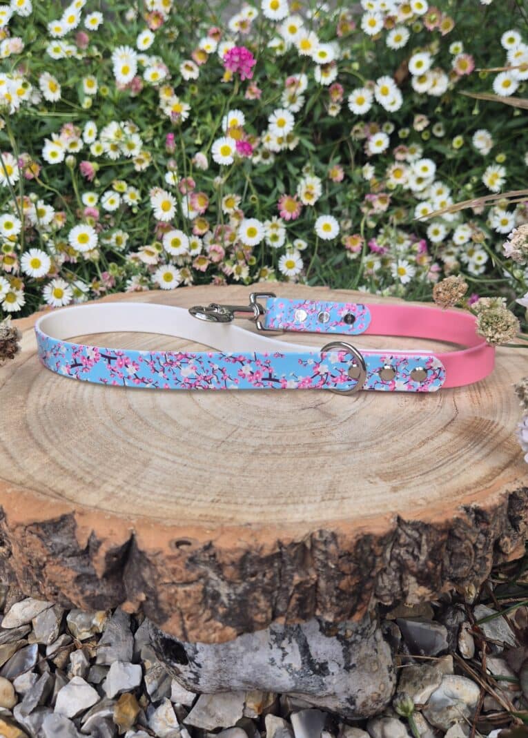 Handmade BioThane dog lead with blue floral print and pink reverse, displayed on wooden log amongst daisies.