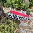 Handmade BioThane dog collar with cow print and pink design, displayed on succulents in a garden setting.