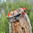Vibrant handmade BioThane dog collar with orange and black dragon design on weathered wood log.