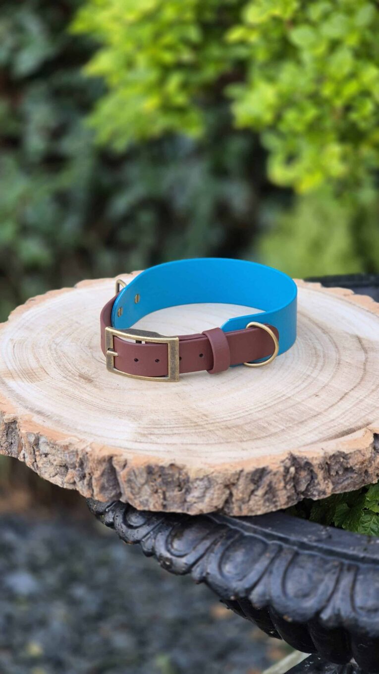 Handmade BioThane dog collar in driftwood and blue with antique brass buckle, displayed on wood.