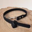 Black BioThane dog collar with textured grip surface and metal clasp, displayed on natural wood.
