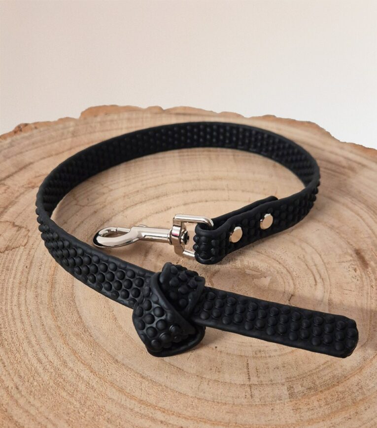 Black BioThane dog collar with textured grip surface and metal clasp, displayed on natural wood.