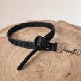 Black handmade BioThane dog collar with grip tag attachment and metal clasp on wooden surface.