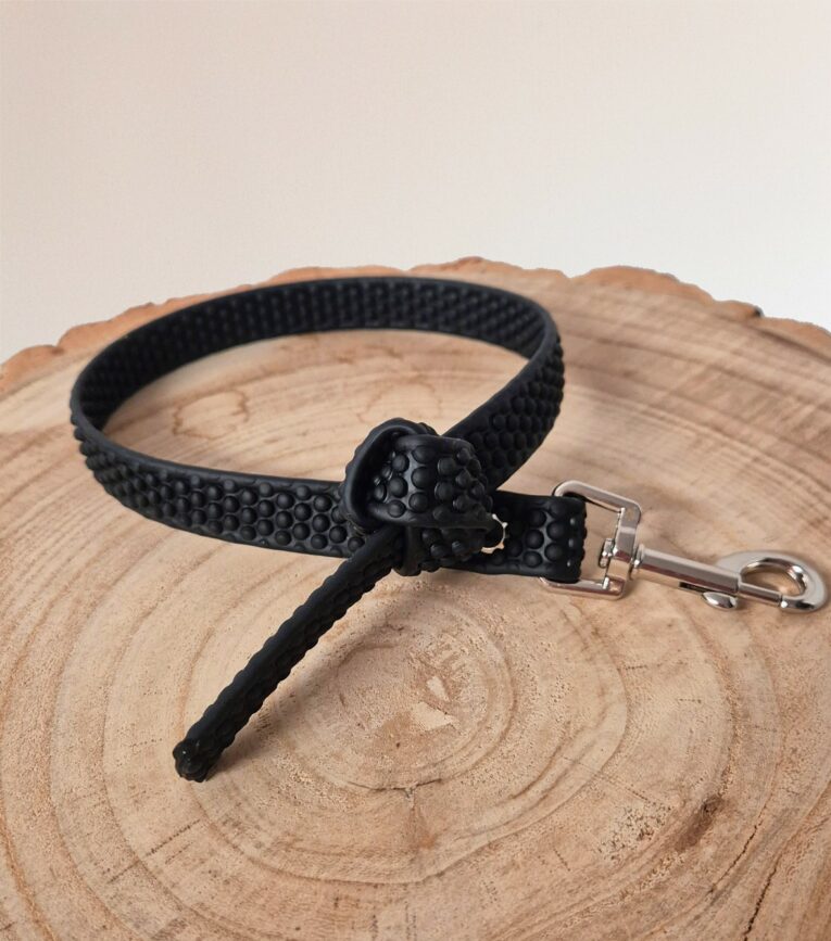 Black handmade BioThane dog collar with grip tag attachment and metal clasp on wooden surface.