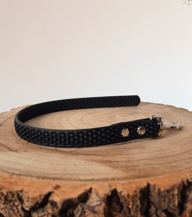 Black BioThane grip tag collar with metal hardware on wooden surface.