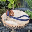 Navy BioThane dog lead with brass hardware and brown handle, displayed on wood slice in garden setting.
