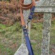 Tan BioThane dog lead with navy handle and brass fittings, draped over weathered wooden fence.
