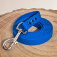 Bright blue BioThane dog lead with metal clasp and adjustment tabs, coiled on natural wood backdrop.