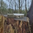 Handmade BioThane dog tag collar in camouflage print with silver hardware, displayed on weathered wood.