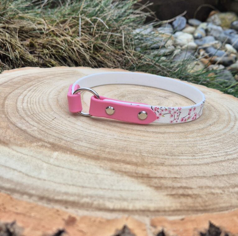 Pink and white handmade BioThane dog tag collar with metal D-ring and studs on wooden surface.