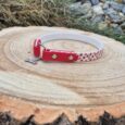 Red and white handmade BioThane tag collar with metal fittings, displayed on a wooden log.