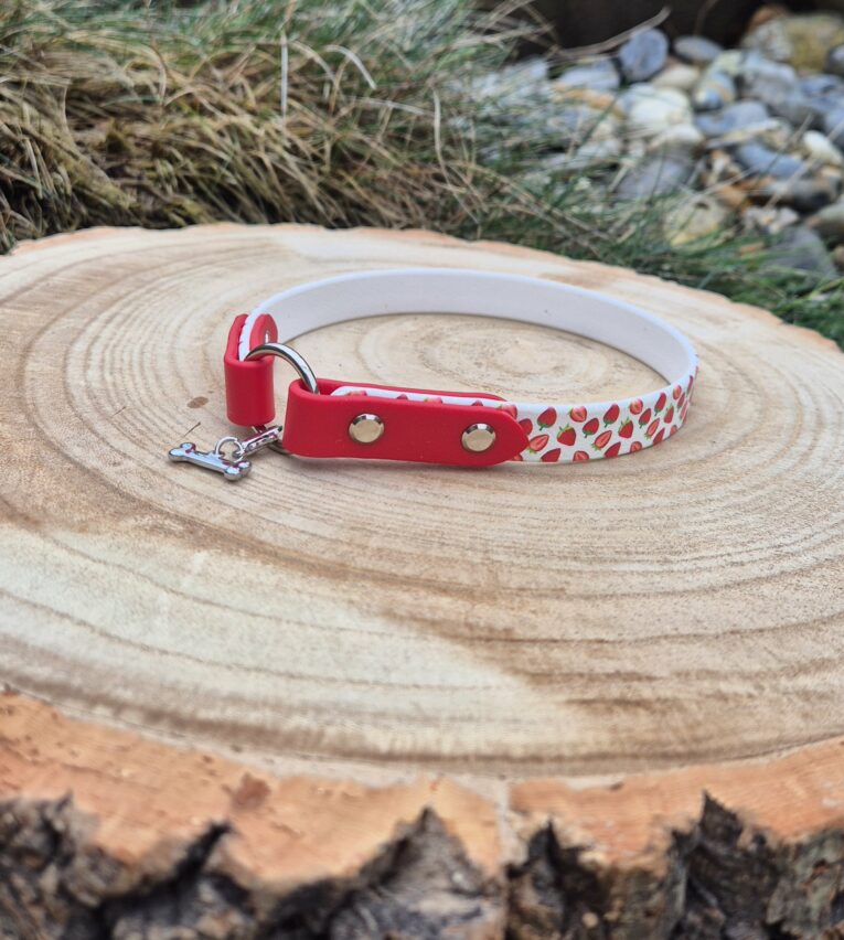 Red and white handmade BioThane tag collar with metal fittings, displayed on a wooden log.