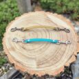 Two handmade BioThane dog collar safety clips with metal hardware displayed on a wooden log cross-section.