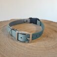 Handmade BioThane dog collar in pale blue with grey lining, metal buckle and D-ring, displayed on wooden surface.