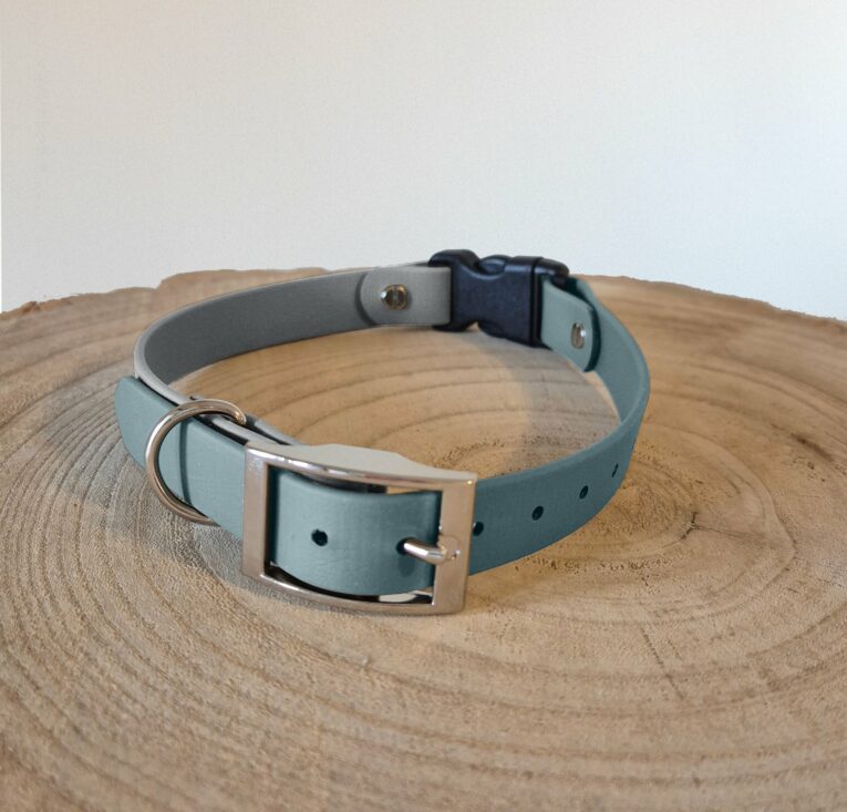 Handmade BioThane dog collar in pale blue with grey lining, metal buckle and D-ring, displayed on wooden surface.