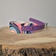 Handmade BioThane dog collar with purple strap and multicoloured geometric print design on wooden surface.