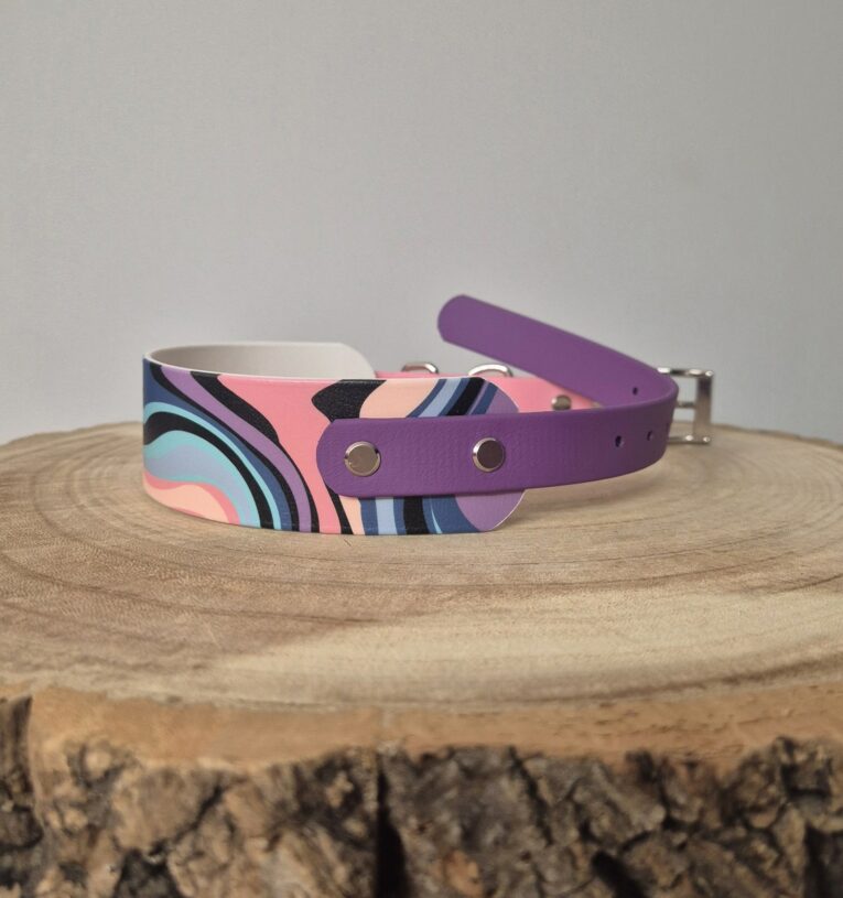 Handmade BioThane dog collar with purple strap and multicoloured geometric print design on wooden surface.