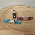 Three handmade BioThane quick release buckles in black, burgundy, and turquoise displayed on a wooden cross-section.