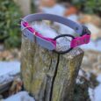 Handmade BioThane dog collar in pink and grey with black ring, displayed on weathered wood.