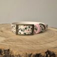 Handmade BioThane dog collar with camouflage print pattern, brass buckle and pink detailing on wooden surface.