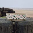 Handmade BioThane dog collar with camo hound design displayed on weathered wooden post by beach.
