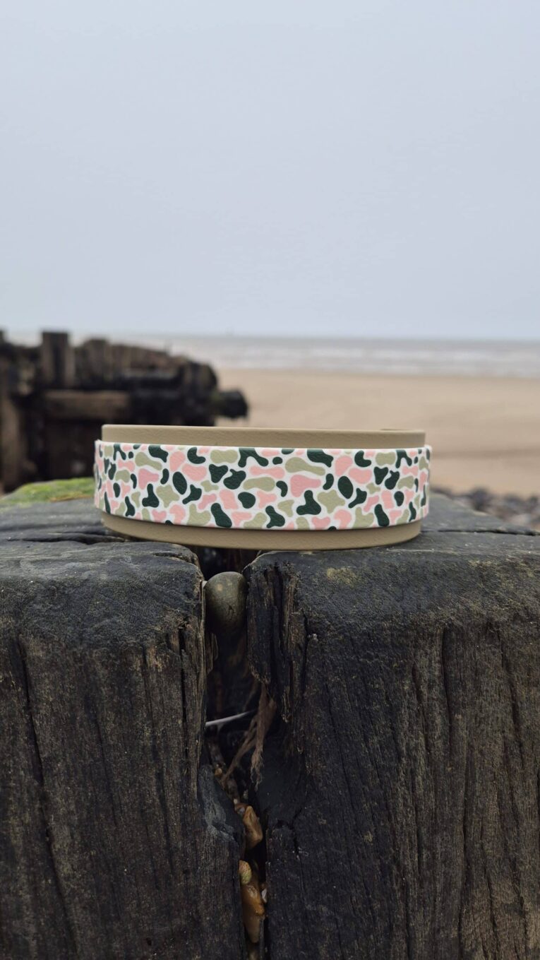 Handmade BioThane dog collar with camo hound design displayed on weathered wooden post by beach.