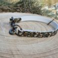 Camouflage slip collar with brass fittings and D-ring, displayed on wooden surface with natural background.