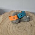 Two handmade BioThane dog collars in vibrant orange and turquoise displayed on textured wood and stone.