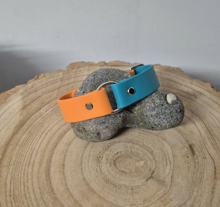 Two handmade BioThane dog collars in vibrant orange and turquoise displayed on textured wood and stone.
