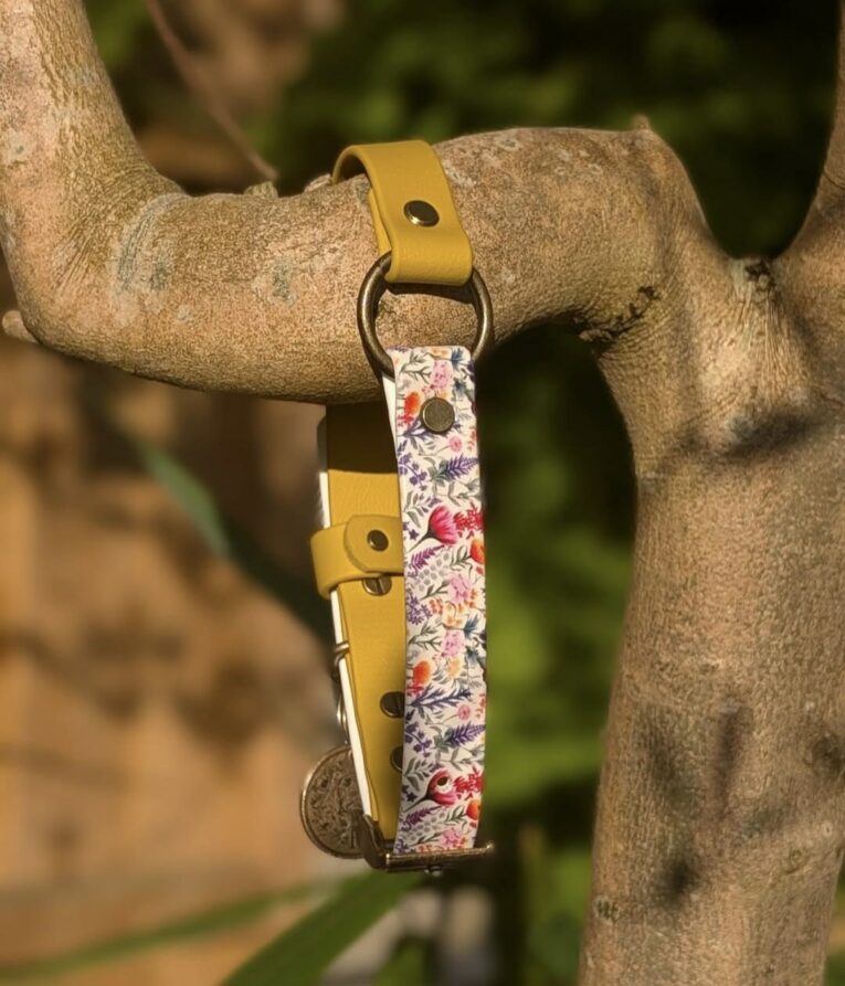 Yellow BioThane gundog collar with floral printed centre section and metal fittings, displayed on wooden branch.