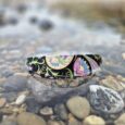 Handmade BioThane dog collar with floral waterproof design, positioned on pebbles by the shore.