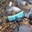 Handmade forest print dog collar positioned on pebbles and stones, showcasing turquoise woodland design with layered evergreen trees.