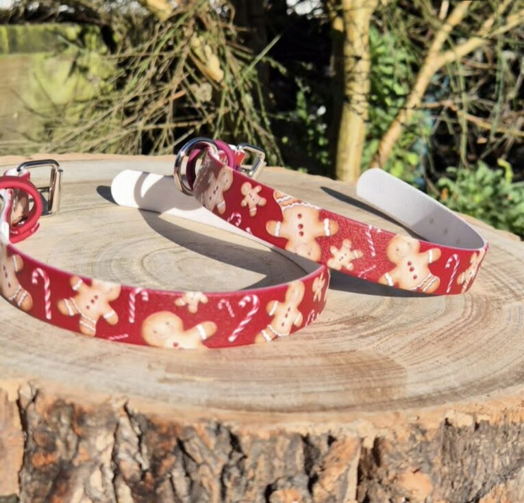 Festive gingerbread man printed handmade BioThane dog collars displayed on wooden log outdoors.