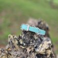 Turquoise polka dot handmade BioThane dog collar with metal hardware displayed on weathered wood outdoors.