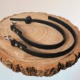 Black handmade BioThane dog collars and leads displayed on natural wood, featuring metal hardware and grip sections.