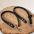 Two handmade BioThane dog leads with textured black grip handles, metal clasps, and decorative studs on natural wood.