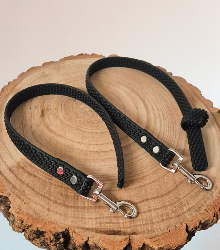 Two handmade BioThane dog leads with textured black grip handles, metal clasps, and decorative studs on natural wood.