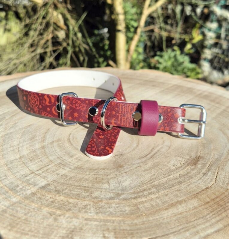 Red Halloween-themed handmade BioThane dog collar with printed design, displayed on wooden surface outdoors.