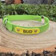 Bright lime green BioThane dog collar with yellow name tag reading 'BUD' displayed on wooden log in garden setting.