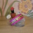 Leopard print handmade BioThane dog collar with vibrant pink band and silver hardware, displayed on glass container.