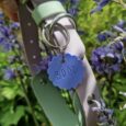 Handmade BioThane hound collar in lilac and sage with blue pet ID tag labelled 'BRÓD', displayed among purple flowers.