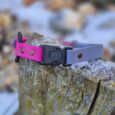 Bright pink and purple handmade BioThane dog collar with black buckle, displayed on weathered wood outdoors.