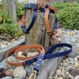 Navy and tan handmade BioThane dog collar and lead displayed in a garden setting with weathered wood.