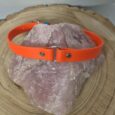 Bright orange handmade BioThane dog collar with metal D-ring and hardware, displayed on natural stone.