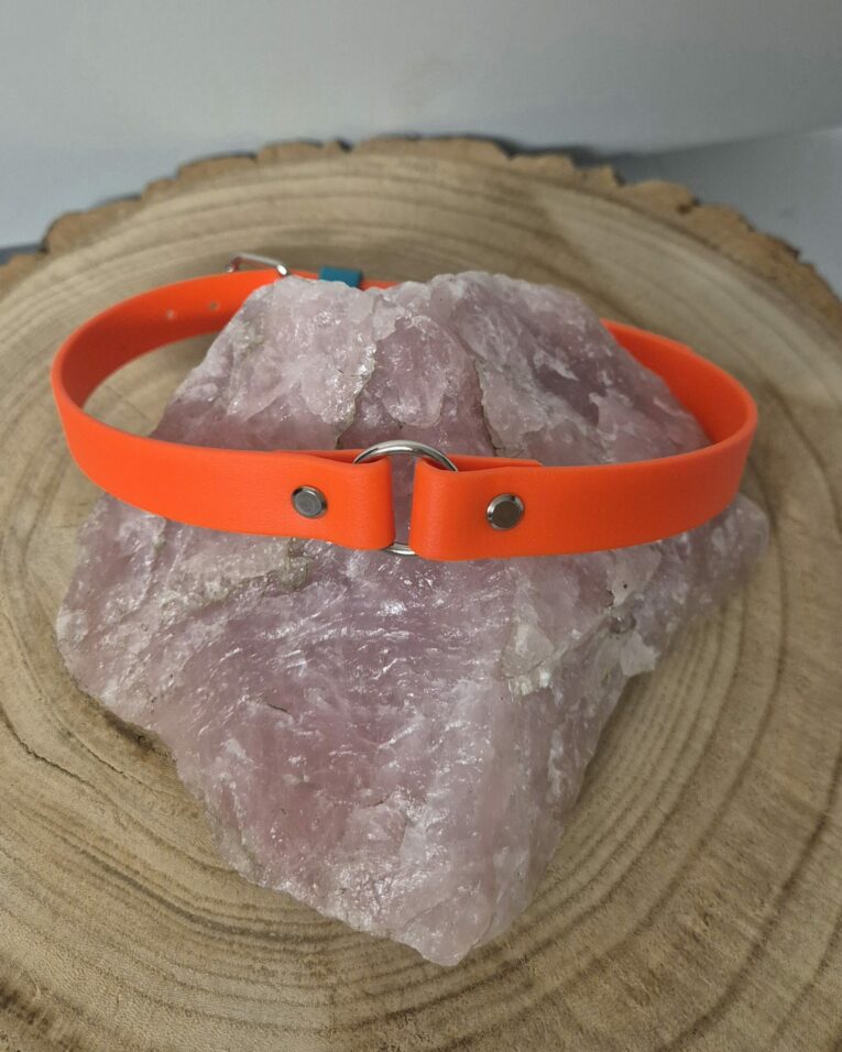 Bright orange handmade BioThane dog collar with metal D-ring and hardware, displayed on natural stone.