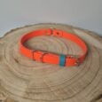 Bright orange handmade BioThane dog collar with teal keeper and metal D-ring, displayed on natural wood slice.
