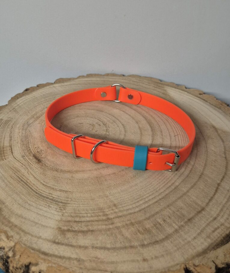 Bright orange handmade BioThane dog collar with teal keeper and metal D-ring, displayed on natural wood slice.