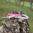 Pink floral handmade BioThane dog lead and solid pink collar displayed on weathered tree stump in countryside setting.