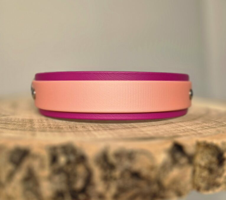 Pink and magenta handmade BioThane dog collar displayed on natural wood surface, showcasing vibrant colour combination and quality craftsmanship.