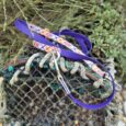 Purple printed BioThane dog lead with colourful woven handle attached to weathered coastal netting.